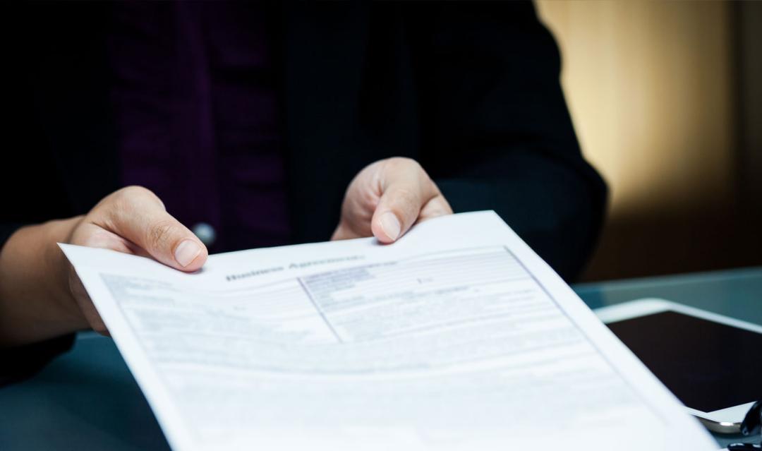 hands holding out a document, inside an office setting