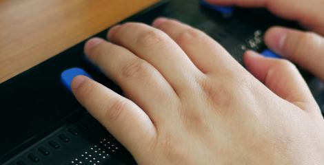 Close-up of a person's hands using computer with braille display