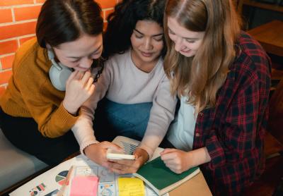 three young women gathered around a table discussing a project