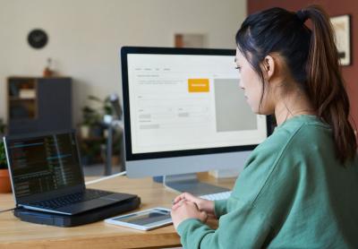 office worker at desk in front of laptop and desktop monitor