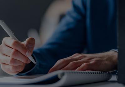 man taking notes with pen and paper, laptop is open 