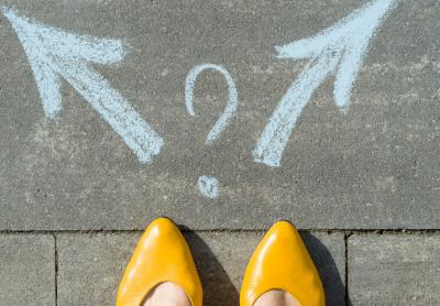 tips of gold shoes on woman's feet, standing before a sidewalk art of two arrows, a decision to be made