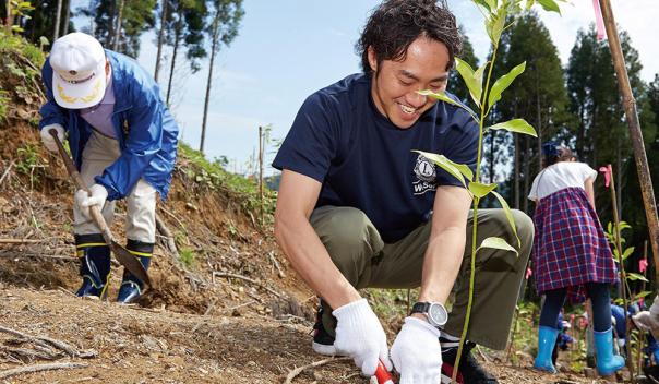 male volunteer helping others with planting, crouching in the dirt of a field