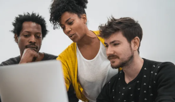 woman in yellow cardigan giving help to two men seated around a computer