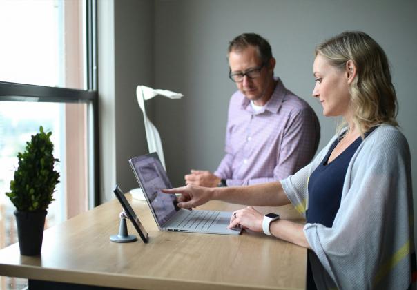 adult man and woman gathered at a standing desk looking at a laptop together