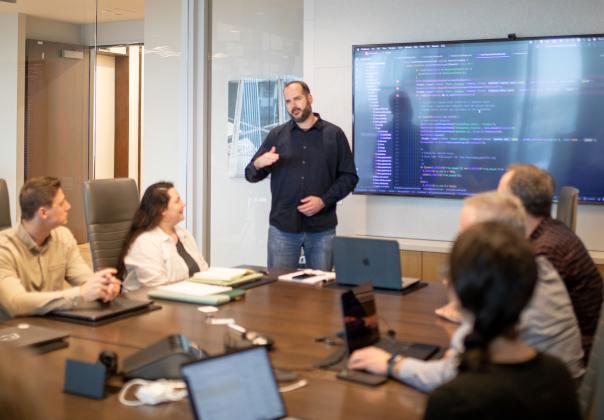 man leading a meeting in a conference room with tv screen behind him
