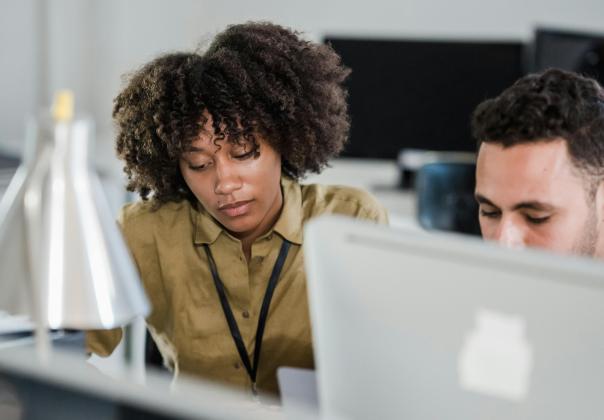 Two adult coworkers huddled around a laptop in an office