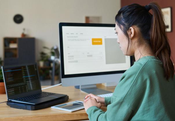 office worker at desk in front of laptop and desktop monitor