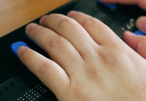 Close-up of a person's hands using computer with braille display