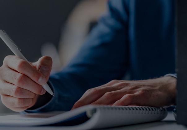 man taking notes with pen and paper, laptop is open 