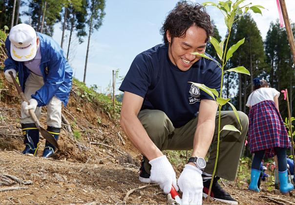 male volunteer helping others with planting, crouching in the dirt of a field