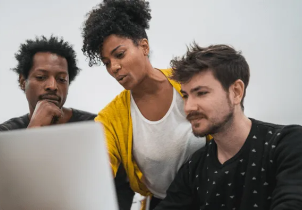 woman in yellow cardigan giving help to two men seated around a computer