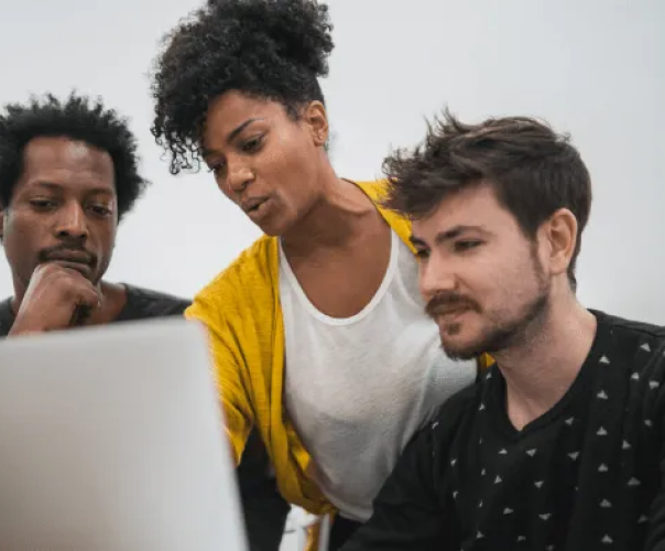 woman in yellow cardigan giving help to two men seated around a computer