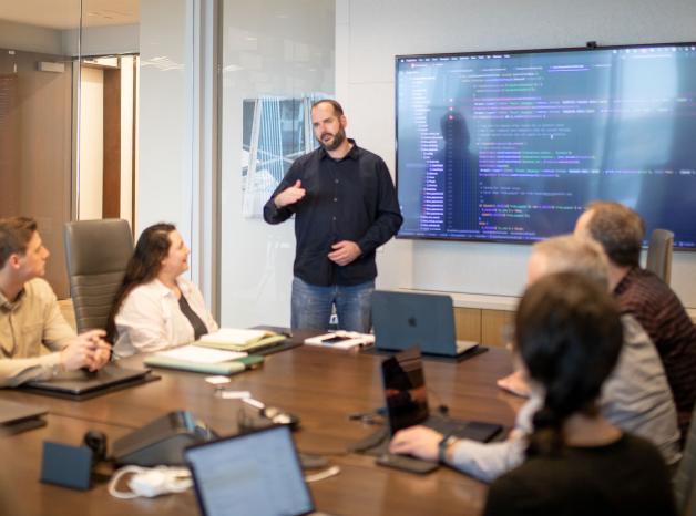man leading a meeting in a conference room with tv screen behind him