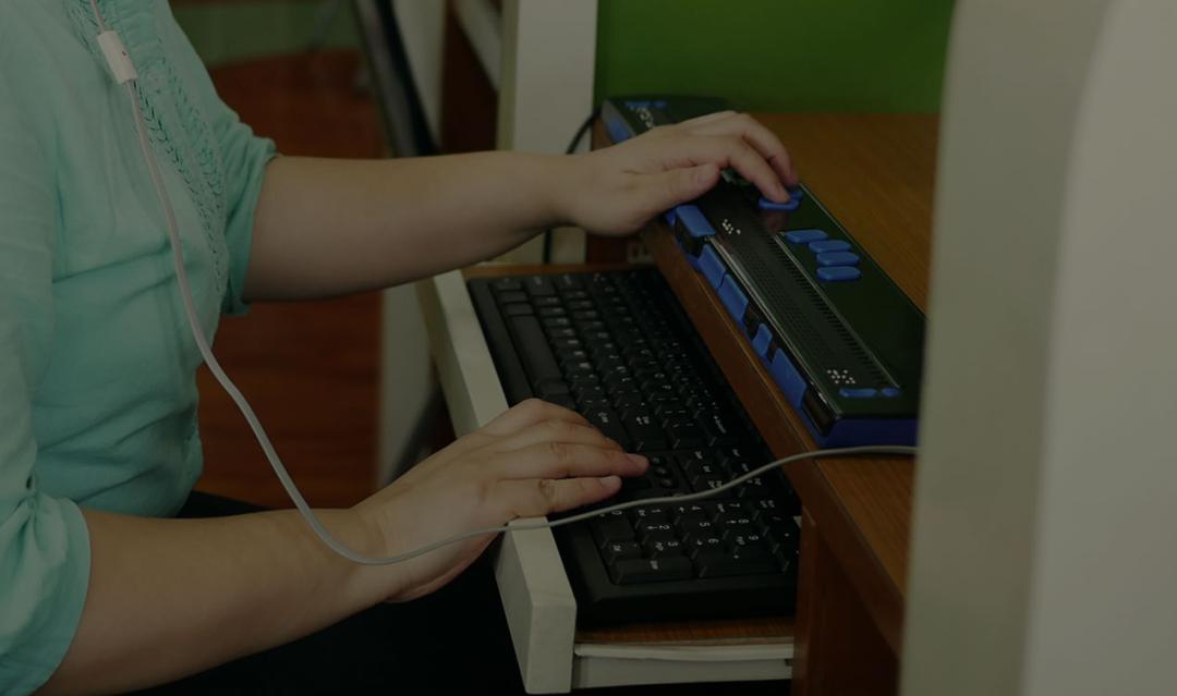 Asian woman with blindness disability using computer with braille in workplace