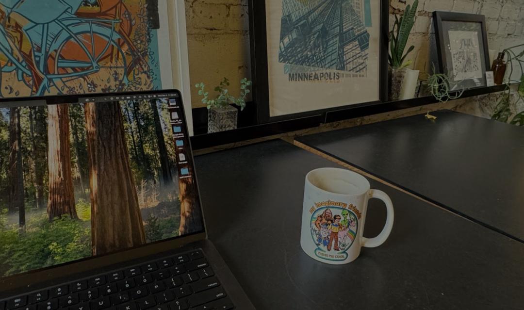 laptop and coffee mug on desk with framed pictures in the background