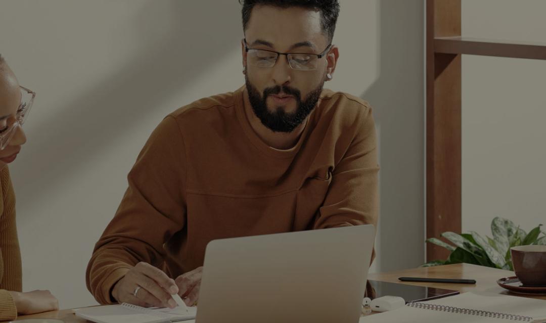 two adults working together at a desk with an open laptop