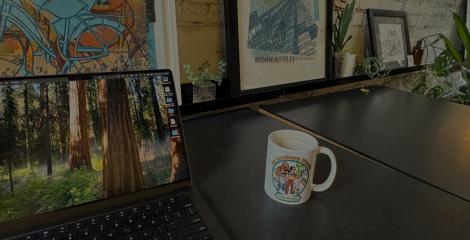 laptop and coffee mug on desk with framed pictures in the background