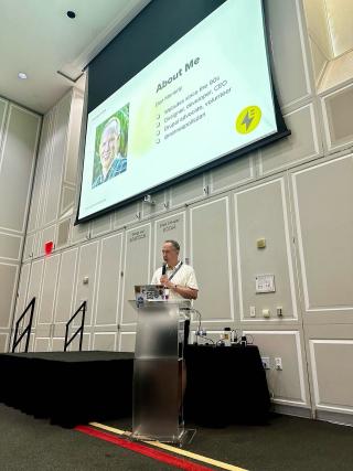 Dan presenting at a conference with a large screen above his head