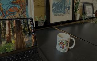 laptop and coffee mug on desk with framed pictures in the background