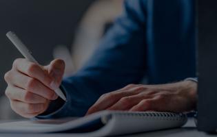 man taking notes with pen and paper, laptop is open 