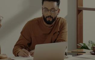 two adults working together at a desk with an open laptop