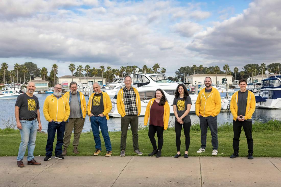 team lined up outside, in front of boats in the bay