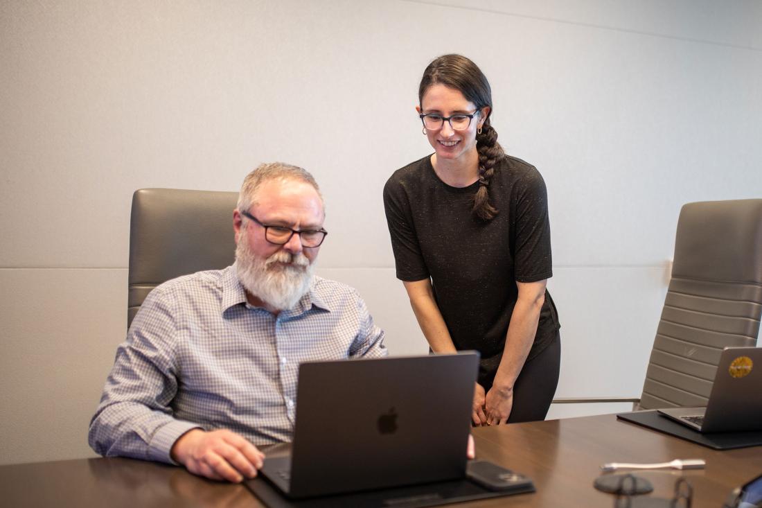 adult man and woman gathered around a conference room table reviewing something on a laptop