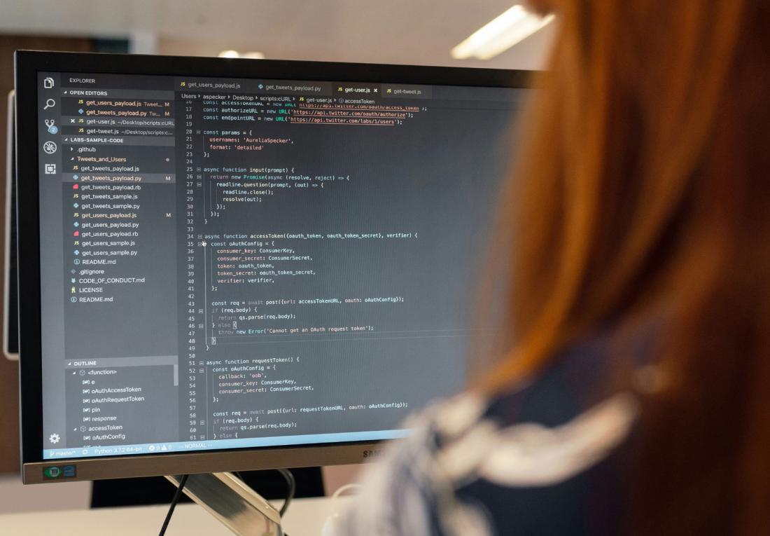 backside view of a person with long red hair looking at a computer screen and code
