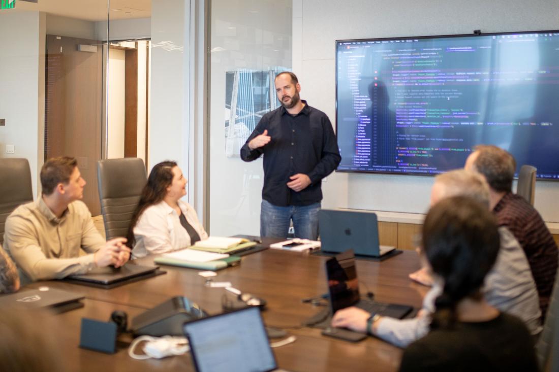 man leading a meeting in a conference room with tv screen behind him