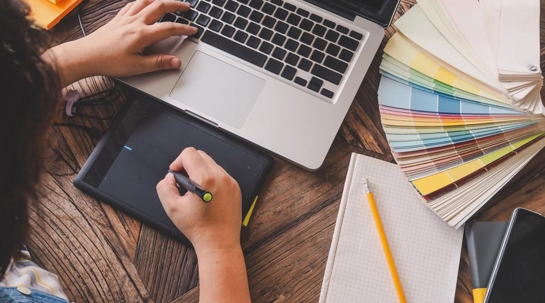image of graphic designer working at desk, surrounded by laptop, color swatches, pen and paper