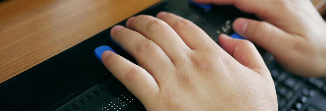 Close-up of a person's hands using computer with braille display